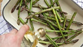 Green asparagus in a roasting tin being drizzled with oil
