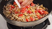 Rice being fried with diced aubergine and tomatoes