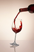 Rotwein aus Flasche in ein Glas gießen