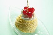 A scoop of vanilla ice cream with redcurrants and a dollop of cream