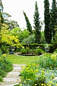 Colourful planters next to pond in front of cypress trees in Mediterranean garden