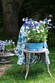 Blue and white summer flowers in old enamel bowl on bistro chair with patterned table cloth hanging over back