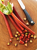 Rhubarb, partially sliced, with a knife on a chopping board