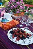 Mixed berries on summery table decked with striped purple cloth and bougainvillea