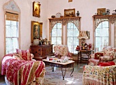 Stilgemixtes Wohnzimmer mit klassischen, floralen Polstermöbeln und antiker Kommode unter barocken Gemälden