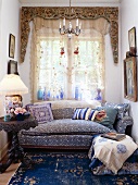 Stilgemixte Wohnnische in Blautönen mit klassischem Sofa und massivem Eisentisch vor Fensterfront mit aufwendig ornamentierter Verblendung