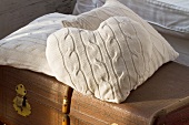 Various cushions with white knitted covers on old trunk