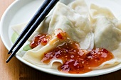 Steamed Dumplings with Red Chili Sauce on a Plate with Chopsticks