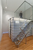 Stainless steel staircase next to glass and steel installation below landing with glass walls