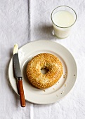 A sesame seed bagel, a butter knife and a glass of milk