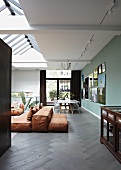 Rust-coloured floor cushions on dark herringbone floor in open-plan interior with skylight