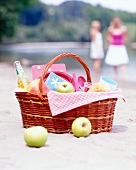 A picnic basket filled with apples, lemonade and baguettes on the beach