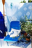 Knallblaue Sonnenliege vor Batik-Tuch als Sichtschutz und Tontöpfe mit mediterranen Pflanzen