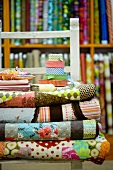 Rolls of patterned fabric on chair in front of shelves of various fabrics