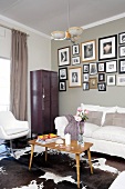 Wohnzimmerecke mit weissen Sitzmöbeln, altem Spind und eingerahmten Fotos an der Wand