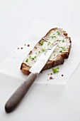 A slice of bread topped with herbs with a knife