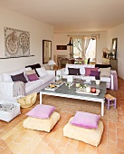 Kissen in Violetttönen auf weissen Sofas in einem hellen, offenen Wohn/Essraum mit Terracottaboden