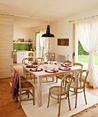 Bentwood chairs with cane seats and simple, rush-bottom chairs at festively set table in front of draped curtains