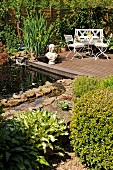 Small pond and wooden deck with bust next to table and garden chairs