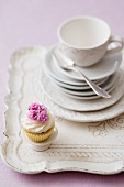 A cupcake on a tray with a stack of plates and a teacup