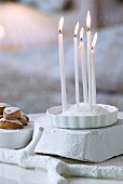 Lit candles stuck into heap of salt in dish on white-painted piece of wood next to pastries