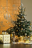 Christmas tree with gold decorations and fairy lights next to gold cube stool