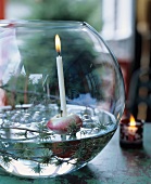 Larch twigs, apples and candle in spherical glass bowl