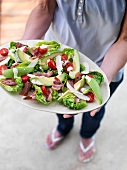 A woman holding a serving platter of avocado salad