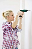 Renovating - woman drilling hole in wall