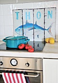 Light blue saucepan on cooker in front of vintage sign with fish motif