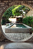View of pool and garden chairs in planted courtyard through circular opening