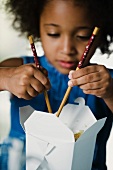 Kleines Mädchen isst asiatisches Essen mit Essstäbchen