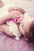A little girl lying on a bed with a soft toy