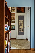 Shelving partition to one side of open doorway leading to hall with view of gallery of picture and Japanese wall hanging on interior door