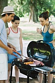Man grilling meats on barbecue while woman and teen girl watch