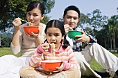 Asiatische Familie isst Nudelgericht im Park