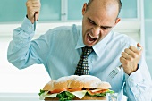Man yelling and attacking large sandwich with knife and fork
