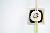Maki-Sushi auf Essstäbchen über Sojasauce