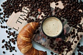 A cup of coffee, a croissant and coffee beans on a newspaper