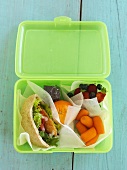 A chicken pita, fruit and vegetables in a lunchbox