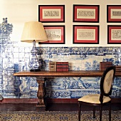 Traditioneller Wandtisch mit Tischlampe vor halbhoch gefliester Wand mit weiss blauen Fliesen und gerahmte Bilder mit Musterausschnitten an Wand