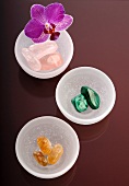 Gemstones in bowls with an orchid flower on a coloured glass surface