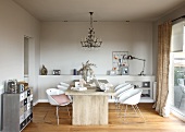 Modern wooden table and white shell chairs below chandelier in simple living room