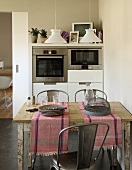 Runners and crockery on rustic kitchen table in front of modern cupboards with fitted appliances