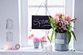 Tulips and twigs of peach blossom in large receptacle, tulips and pink hyacinths in zinc containers and blackboard hanging from window