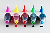 Five Bottles of Food Coloring with Caps Removed and a Drop of Each Color Under Each Bottle