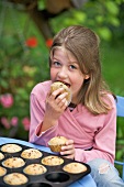 A girl eating muffins at a table in a garden