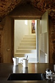 Two coffee mugs next to undermount sink in stainless steel worksurface; view of masonry steps through open door in background