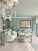 Chandelier and lounge area with white sofa set and modern coffee table against walls painted pale blue in traditional setting