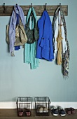 Offene Garderobe - Vintage Wandhakenleiste aus Holz mit Kleidung und Schuhe in Drahtkörben vor hellblau getönter Wand